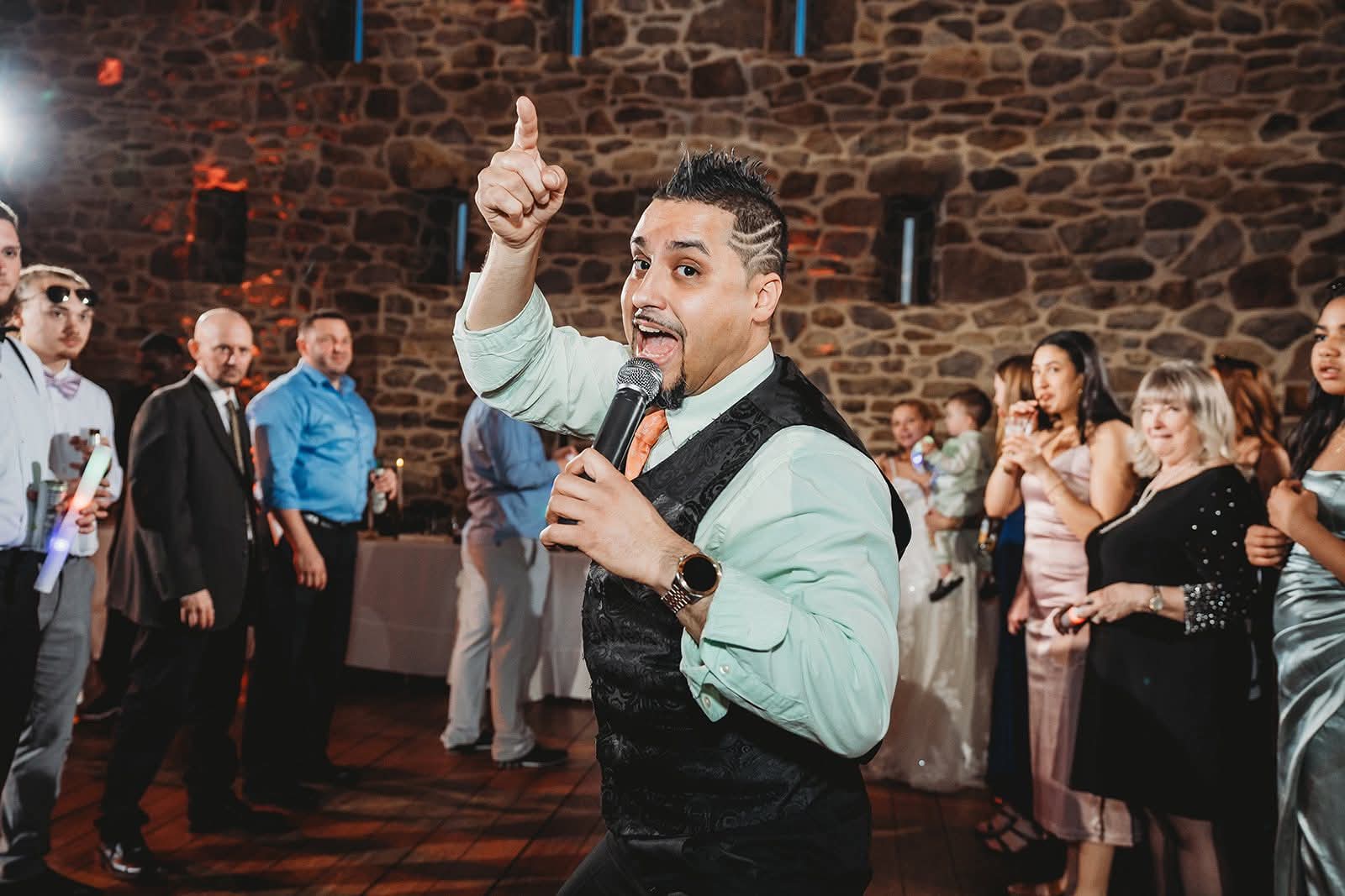 DJ-JP con el micrófono en medio de la pista de baile, señalando hacia arriba, con los invitados a su alrededor